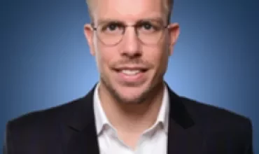 Person wearing glasses and a suit against a blue background.