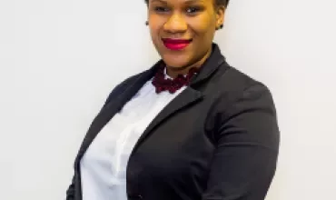 Person in black blazer and white shirt smiling against white background.