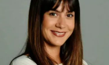Person smiling with long hair on a gray background.