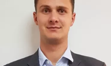 Person in a suit smiling at the camera against a white background.