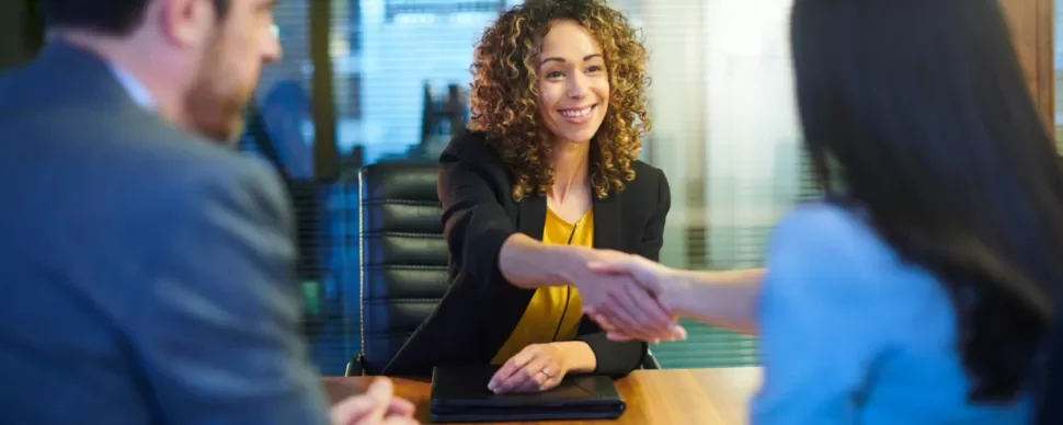 Person smiling and shaking hands across a table during a meeting.