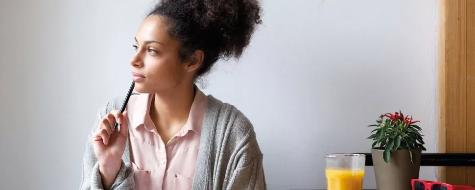 Person sitting at a table with a pen, looking thoughtful.