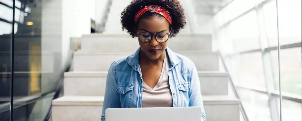 Person sitting on stairs with a laptop and wearing glasses.