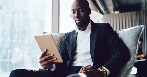 Person in a suit reading on a tablet by a window.