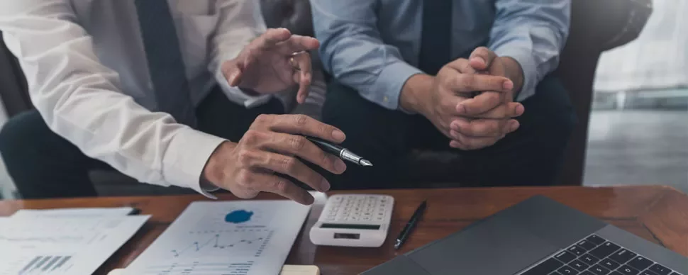 Two people discussing charts and graphs at a table with a laptop.