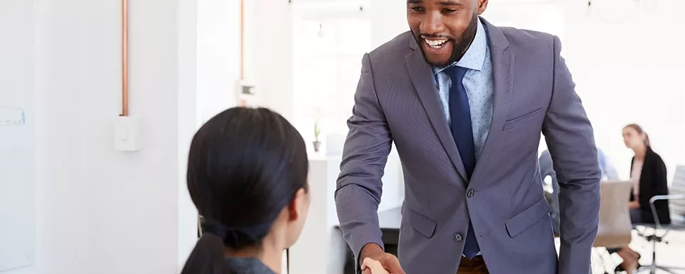 Two people shaking hands in a modern office setting.