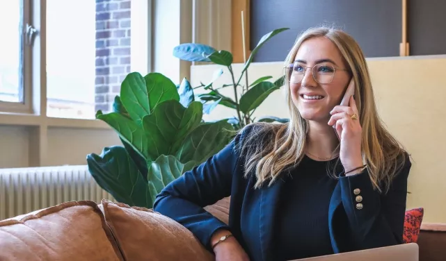 Person smiling while talking on the phone in a cozy room.