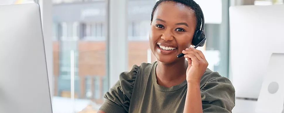 Person smiling at computer with headset in office.