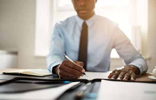 Person writing at a desk with a notebook and pen.