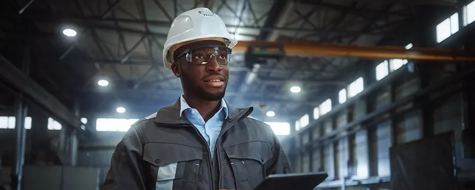 Worker wearing a hard hat and safety glasses in a factory setting.