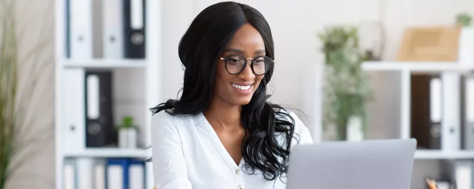 Person smiling while working on a laptop in an office.
