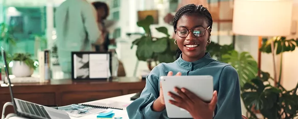 A smilingwoman standing in an office on an ipad 