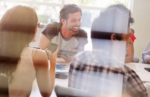 People having a friendly meeting in an office, smiling and using devices.
