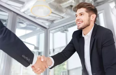 Person in a suit smiling, shaking hands in a modern office.