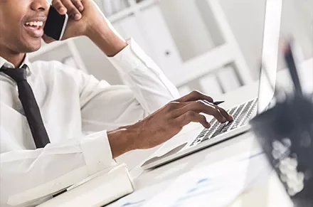 Person on phone using a laptop at a desk.