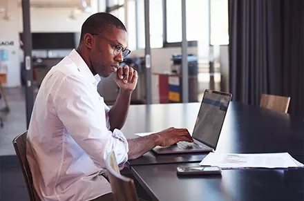 Person working on a laptop at a table with documents.