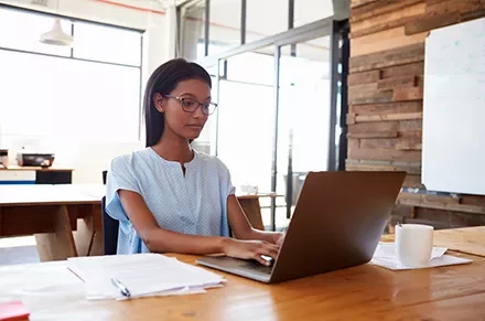 Person working on a laptop at a wooden desk in a modern office.