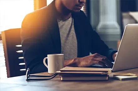 Person working on a laptop with a coffee cup on the desk.