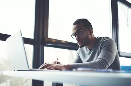 Person working on a laptop at a desk by a large window.