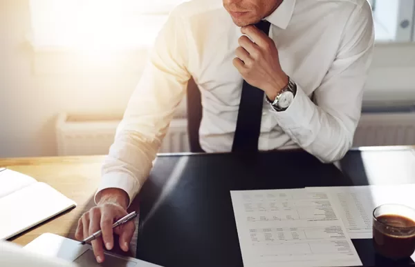 Person in formal attire working on a laptop with documents on the desk.