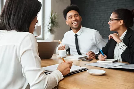 Three people smiling and talking during a meeting in an office setting.