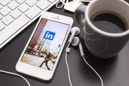 Smartphone with LinkedIn app on screen next to a keyboard and coffee cup.