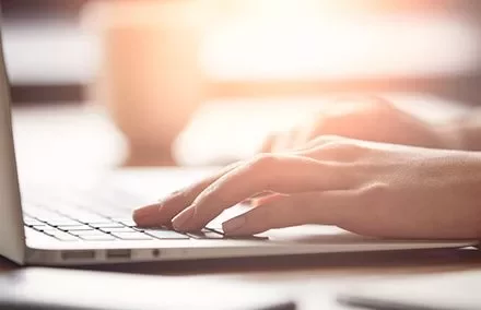 Hands typing on a laptop keyboard in soft lighting.