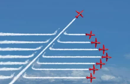 Red planes in formation, one breaking away, leaving white smoke trails against a blue sky.
