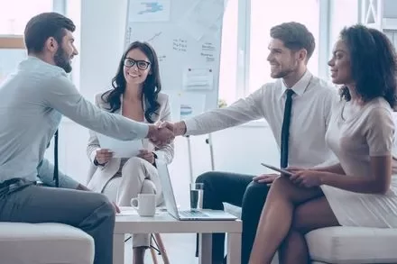 Group of professionals in a meeting, two are shaking hands.